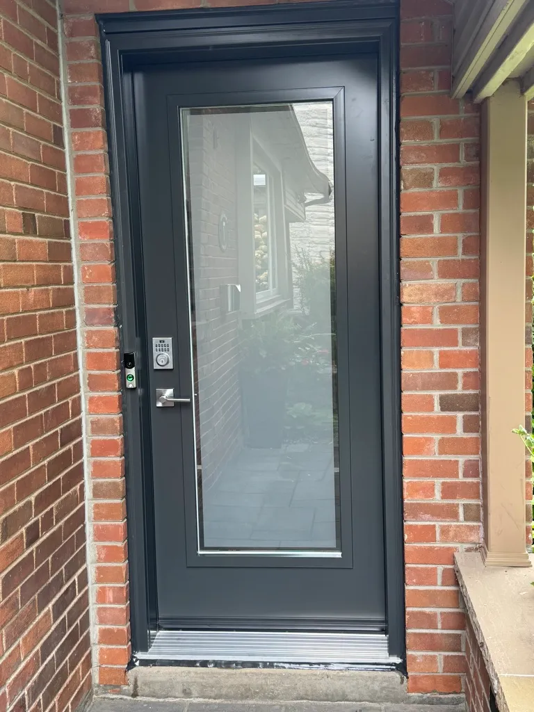 Black entry door with a tall clear glass panel in a brick entrance