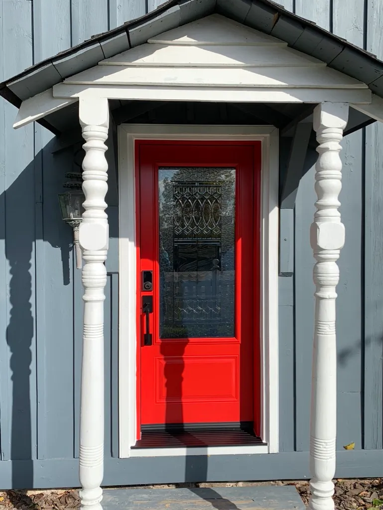 Red entry door with decorative glass beneath a small covered entrance