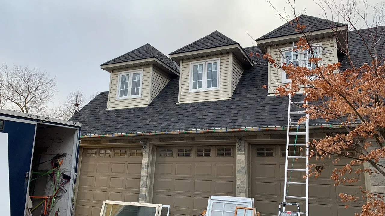 Three white-framed dormer windows above a garage during installation work