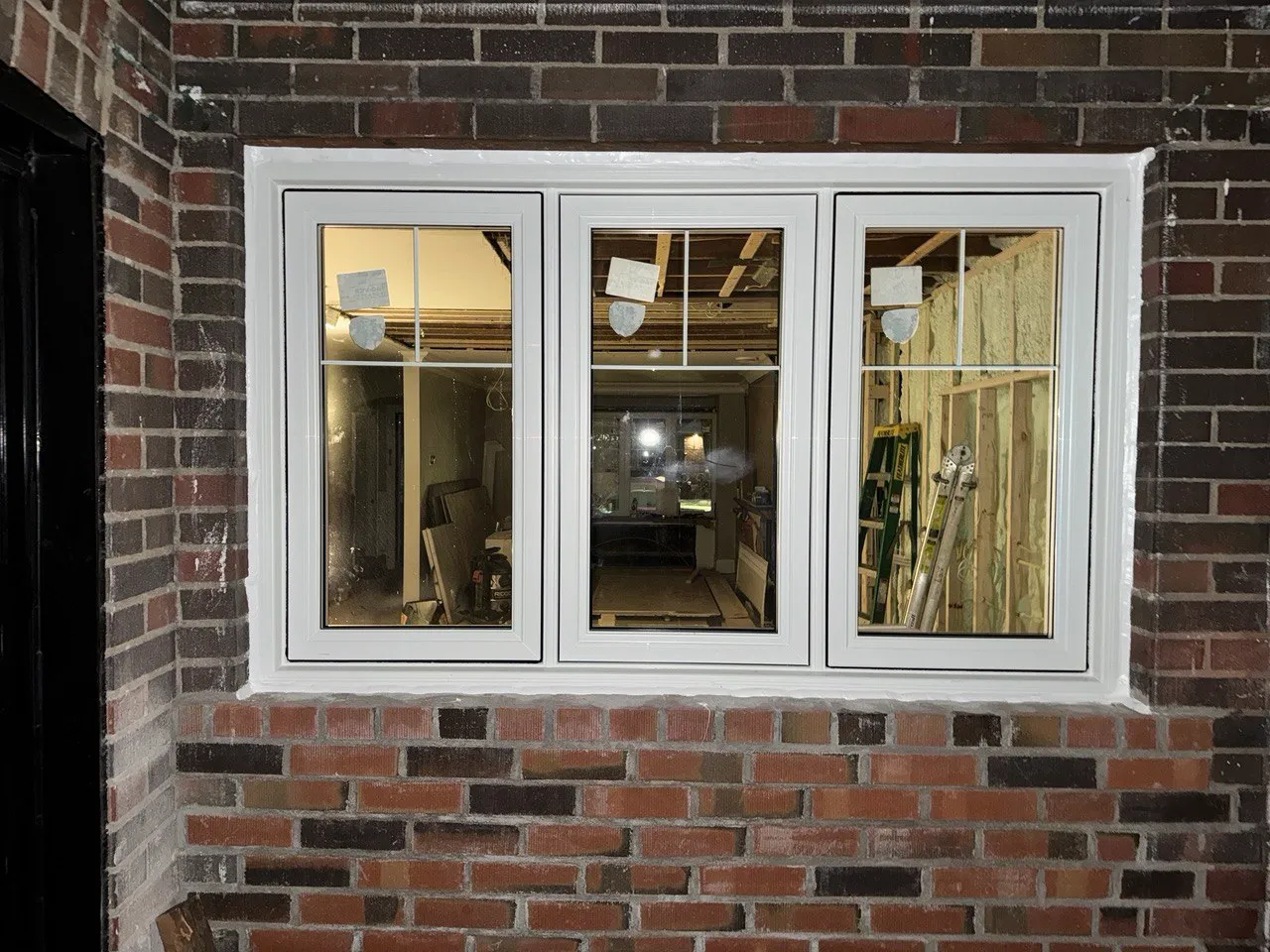 White three-panel window in a dark brick wall